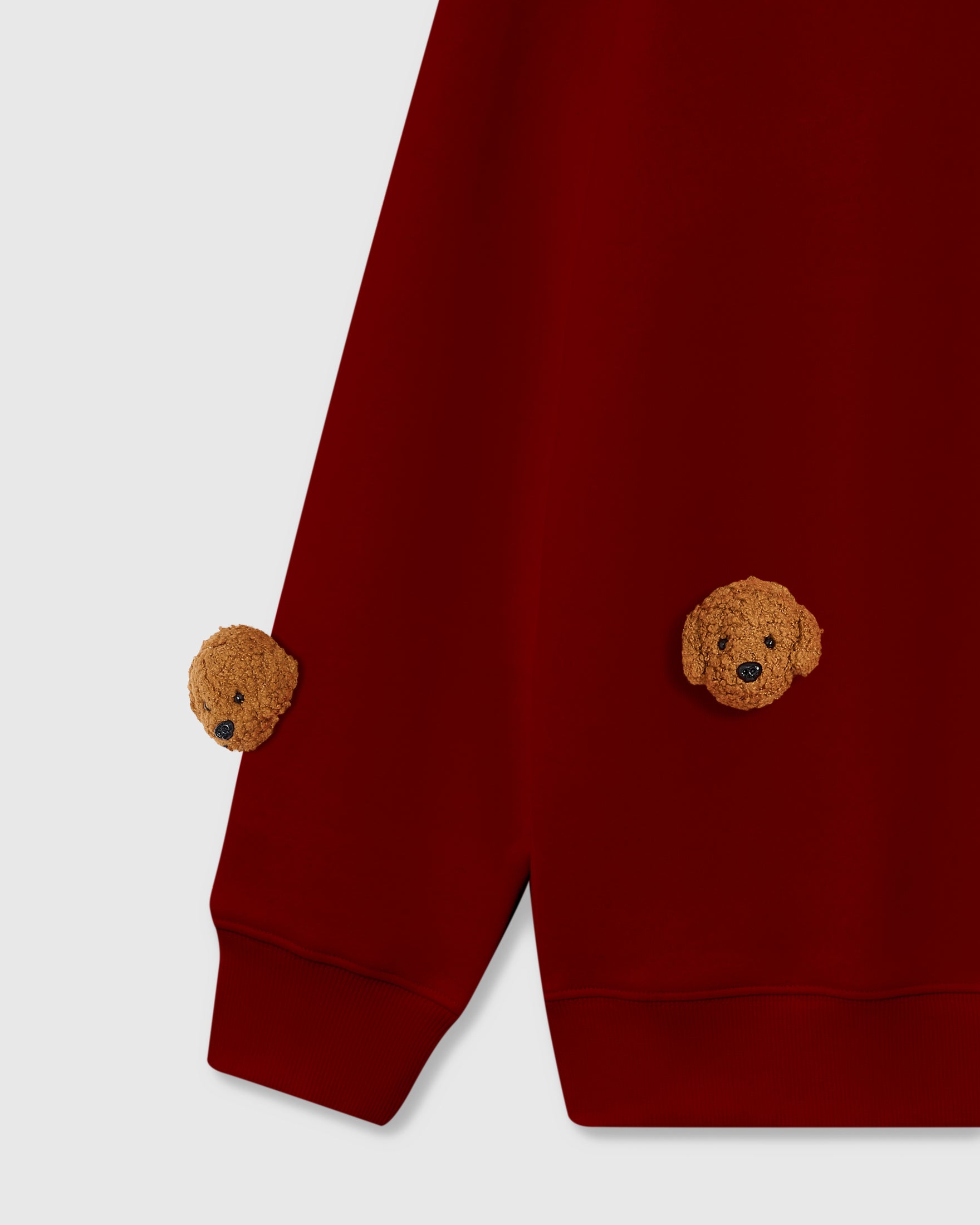 Detail of three hand-stitched poodle faces on burgundy sweatshirt showing dimensional plush against deep red cotton