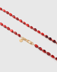 Close-up of ruby red elongated marble-style beads with smoky swirls and gold spacer hardware