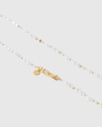 Close-up of irregular baroque faux-pearls and gold-tone ball spacers meeting the gold dual clasps and round engraved disc.