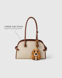 Handmade Cocker Spaniel leather bag charm clipped to a cream canvas handbag — built to last from French Alran leather and suede, hand-layered face panels. STICKYZOO collectible.