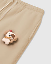 Angled close-up of hand-stitched plush puppy on cream STICKYZOO sweatpant showing layered plush construction near pocket