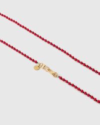 Macro of glossy scarlet resin beads and tiny black spacers meeting a gold-tone clasp and round engraved STICKYZOO disc.