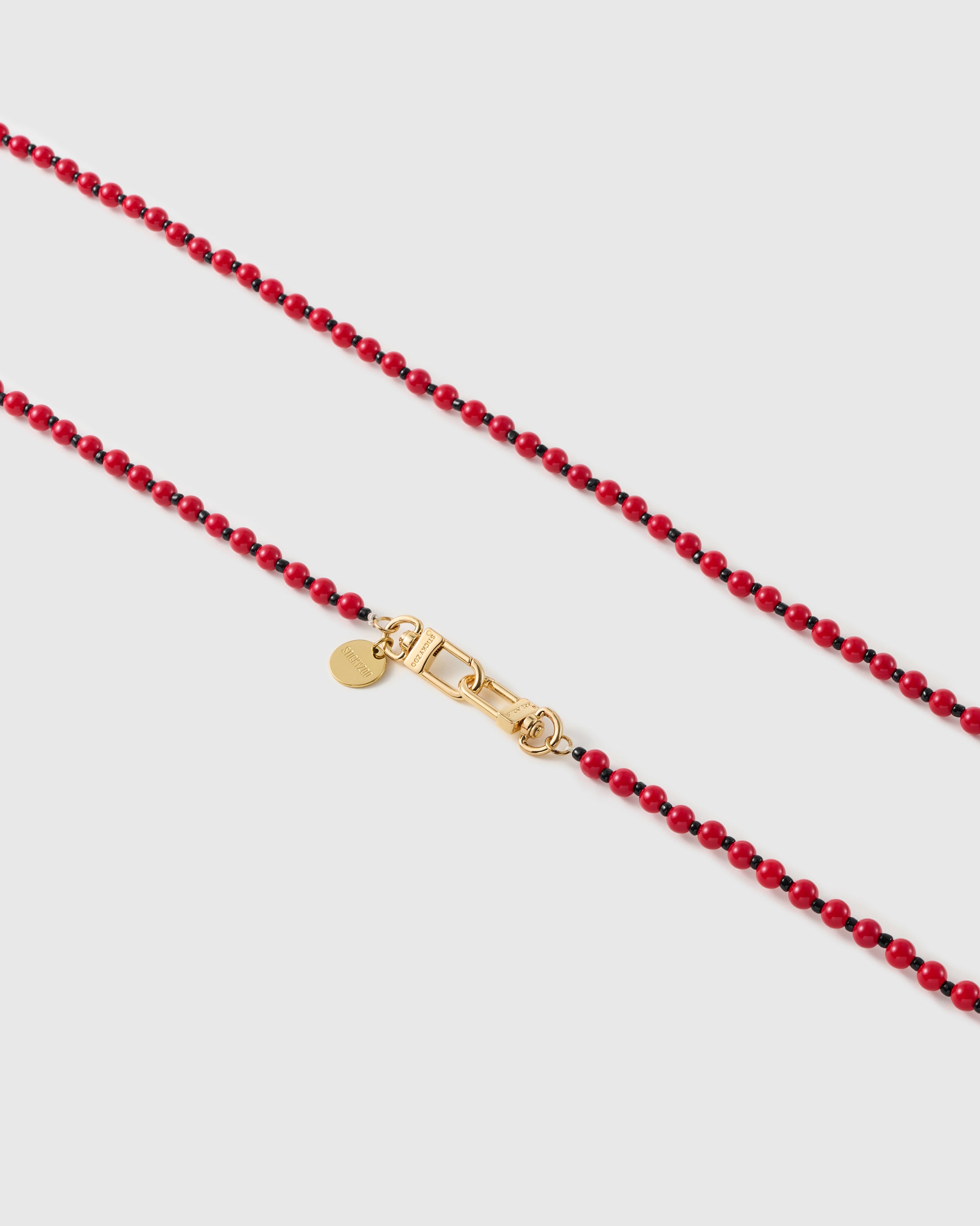 Macro of glossy scarlet resin beads and tiny black spacers meeting a gold-tone clasp and round engraved STICKYZOO disc.