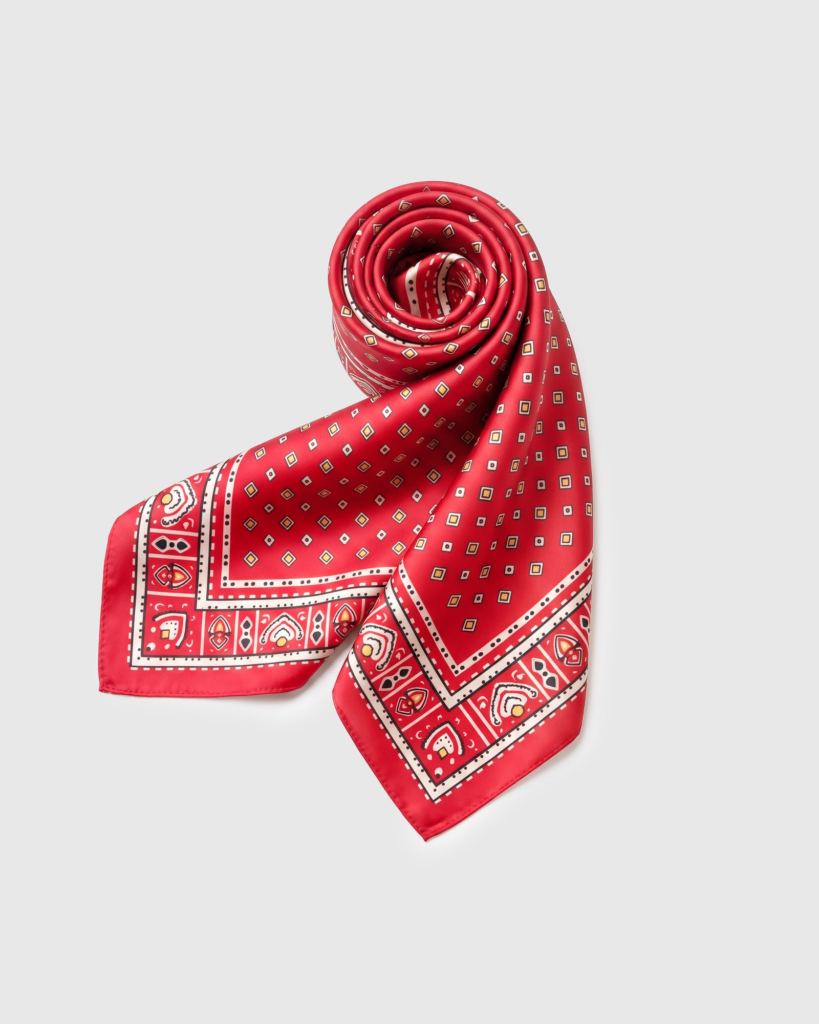 Poppy silk foulard scarf rolled into a fold showing the diamond field and ornate cream border
```