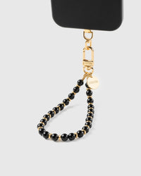 Noir sphere phone strap hanging from black phone case showing wrist carry with gold hardware