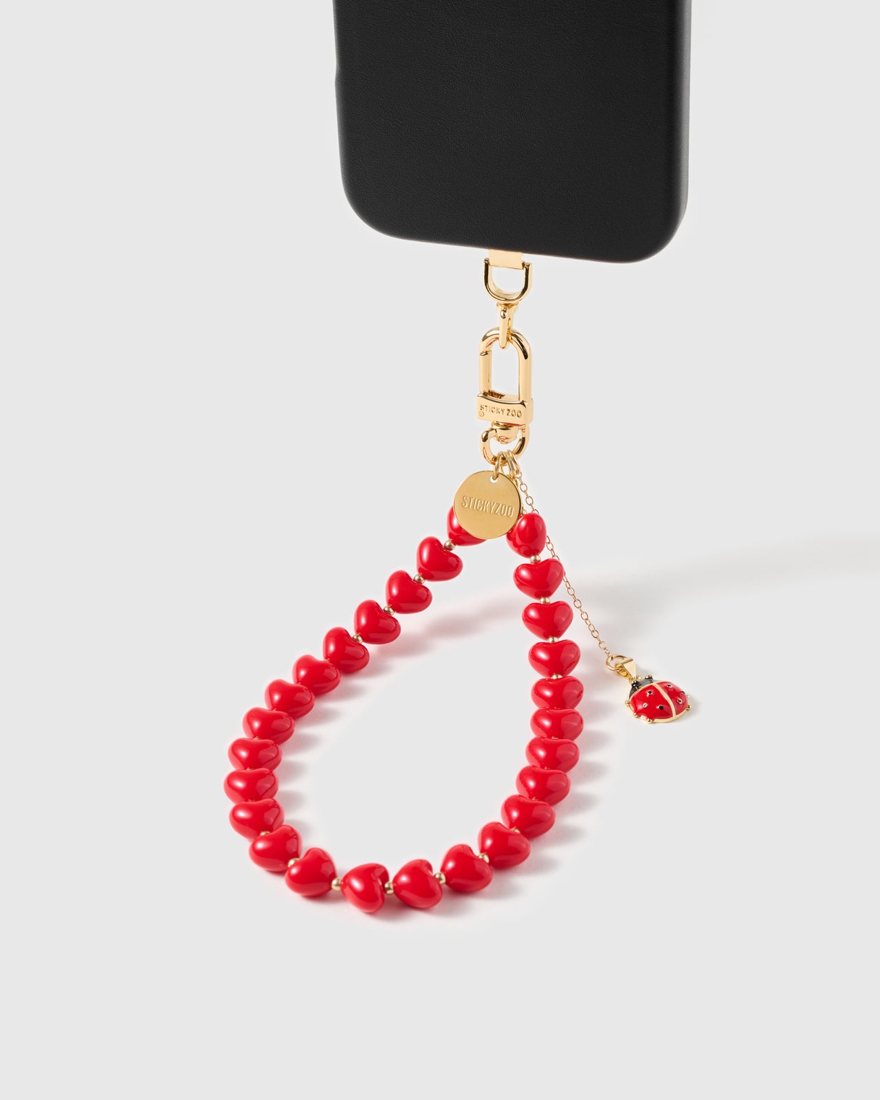 Ladybug charm strap with crimson hearts hanging from phone case showing drop-chain detail