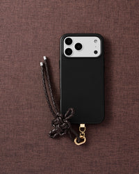 Phone with mocha leather bow strap on dark brown fabric lifestyle flat-lay