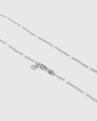 Close-up of silver-tone ball beads spaced with faux-pearls, with the dual silver-tone clasp and small engraved disc at center.
