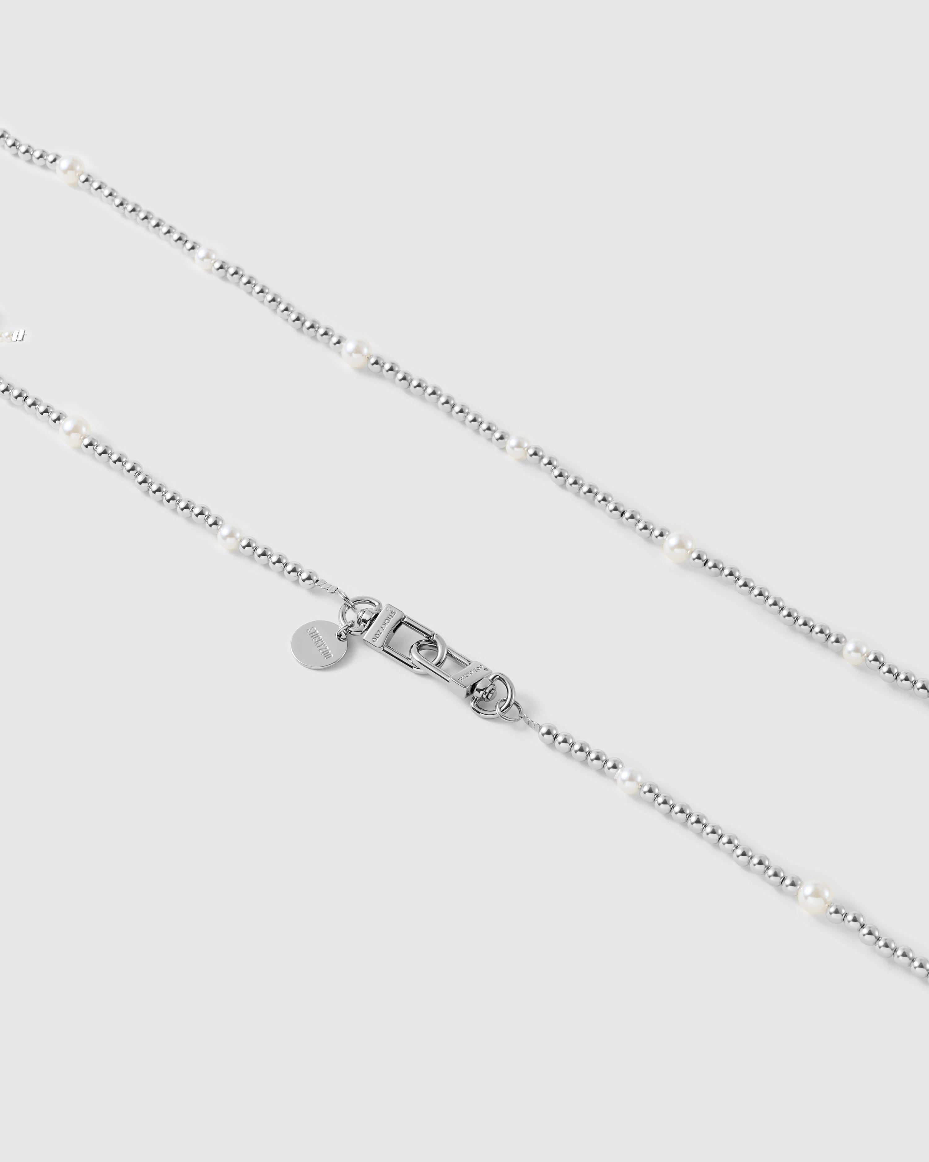 Close-up of silver-tone ball beads spaced with faux-pearls, with the dual silver-tone clasp and small engraved disc at center.