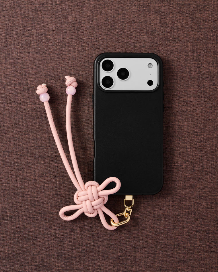 {{Designed in Amsterdam}} Rose knot phone strap on fabric background showing full knot detail and bead-tipped tails