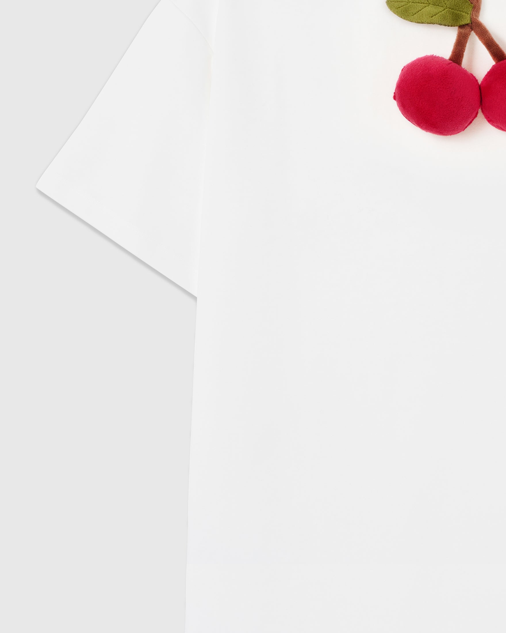 Sleeve and chest detail showing dropped shoulder seam and partial plush cherry appliqué on white cool-touch cotton