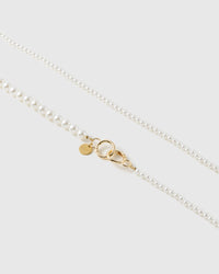 Close-up of the faux-pearl strap where small pearls meet larger ones, beside a gold-tone ring and a small engraved disc