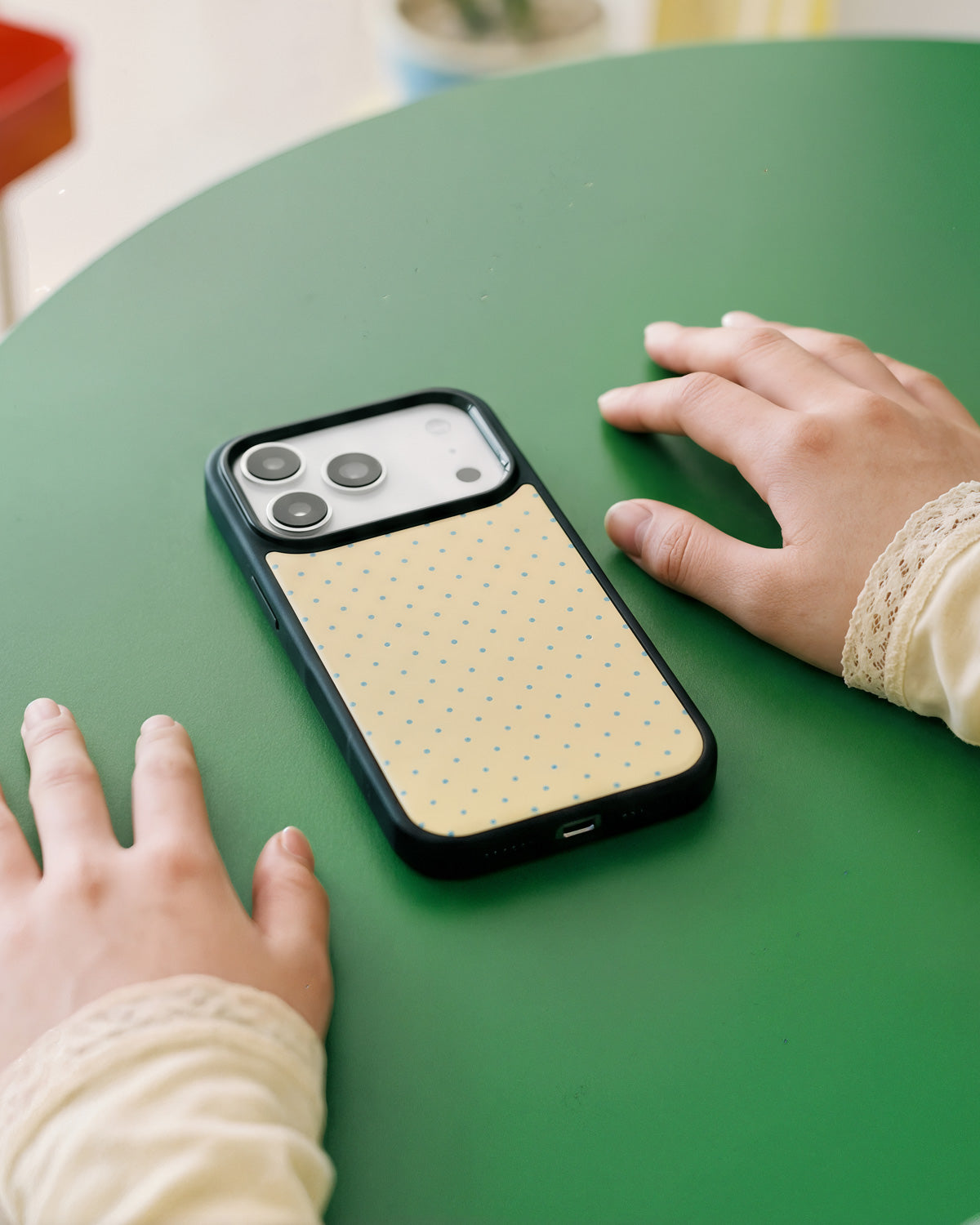 STICKYZOO ginger cat phone case resting on a green café table with the cream polka-dot back facing up