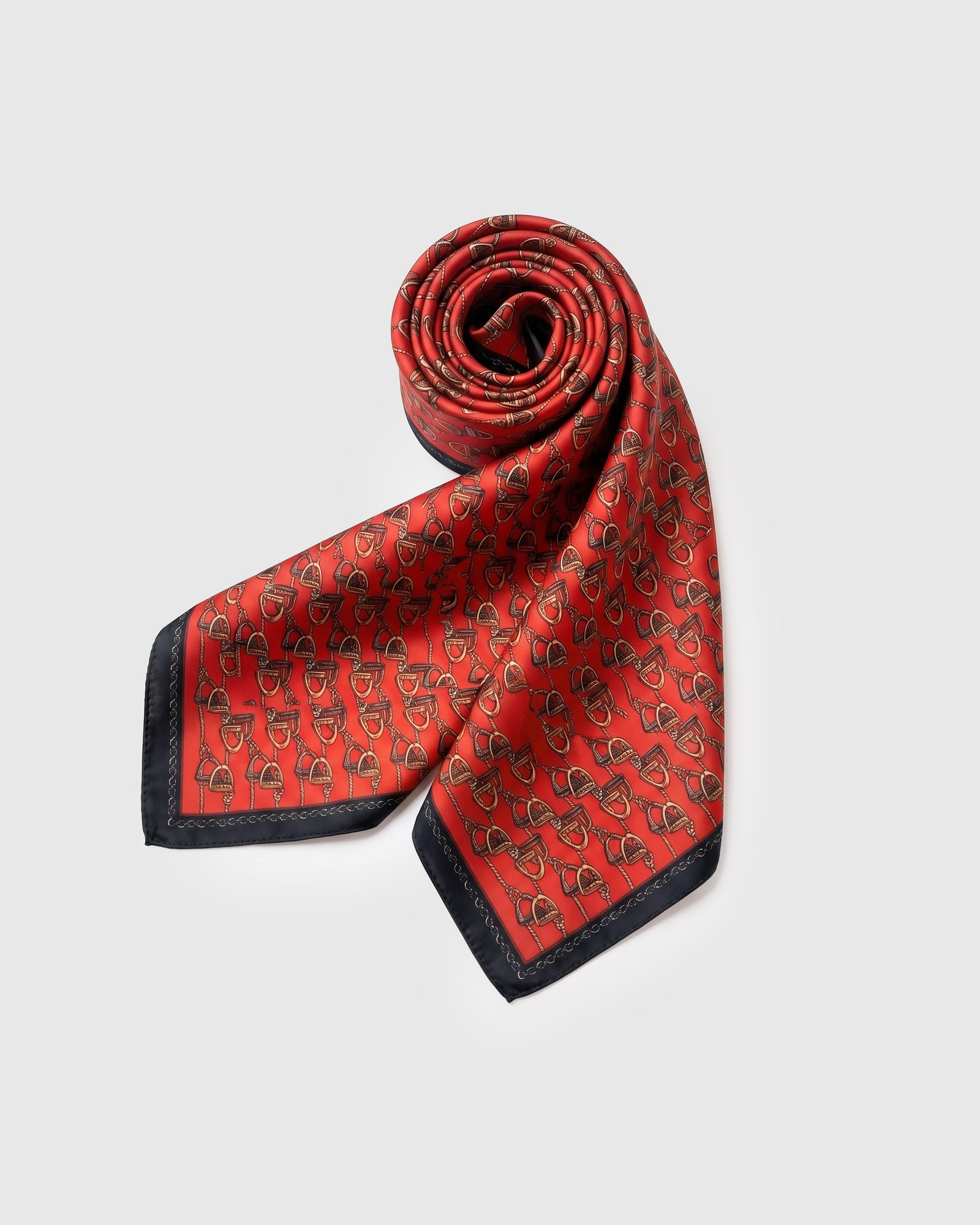 Saddle-red silk equestrian scarf rolled into a soft fold showing the stirrup repeat
```