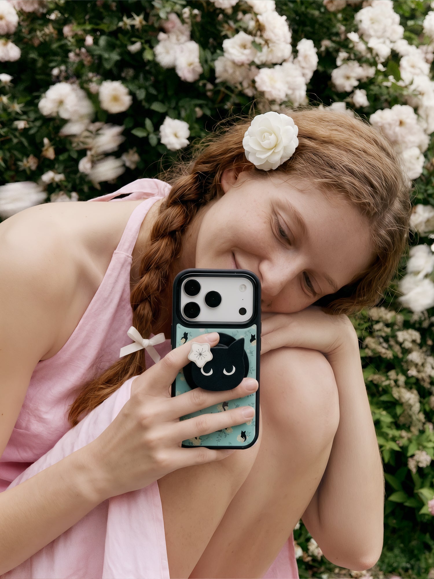 Midnight cat phone case held with fingers around the retractable cat-face MagSafe grip on the back