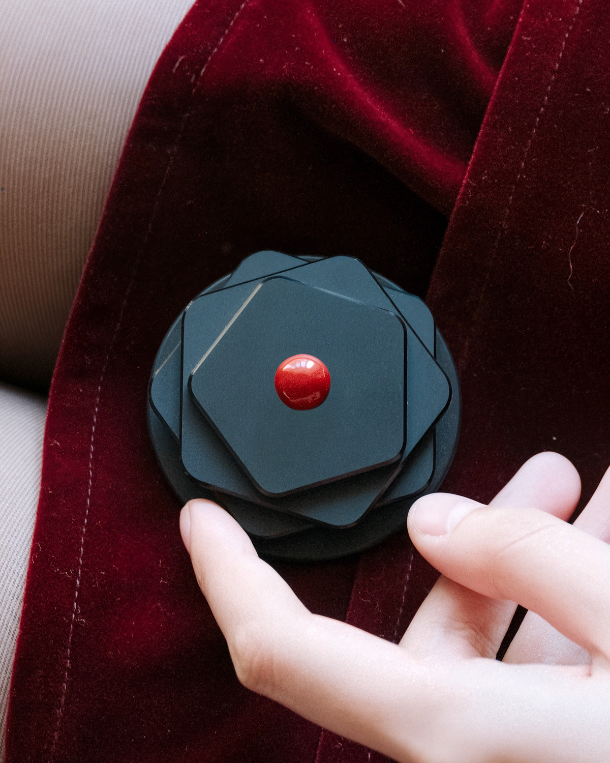 Close-up of the 3D black geometric iris medallion with a red centre bead embedded in the acrylic-resin grip