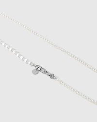 Close-up of round white faux-pearls meeting puffy heart beads beside a silver-tone swivel clasp and a small engraved disc.