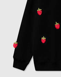 Close-up of plush strawberries scattered across lower front and sleeve cuff on black cotton
