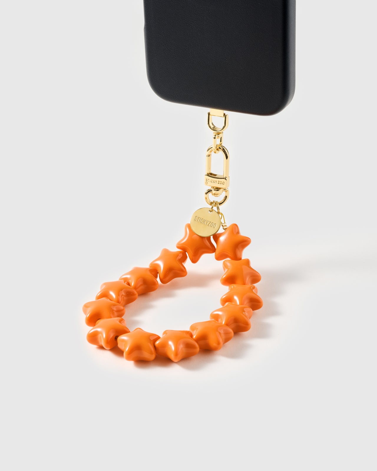 tangerine star phone strap clipped to a black phone case — hands-free wrist carry. Rated 4.9 stars.