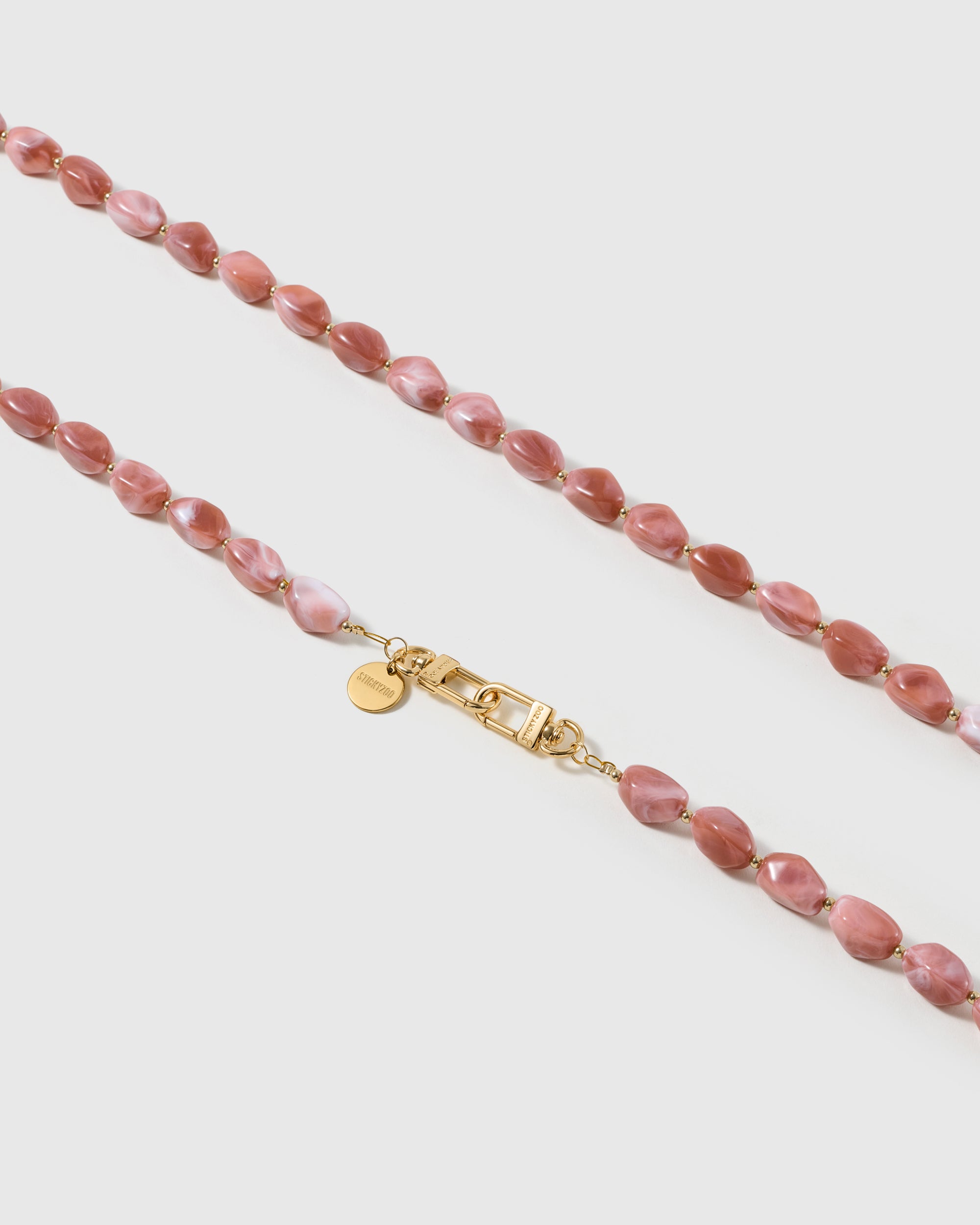 Macro close-up of the polished dusty-rose resin beads and gold-plated clasp, each strap assembled by hand