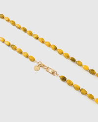 Close-up of golden yellow and olive elongated marble-style beads with gold spacers and engraved hardware