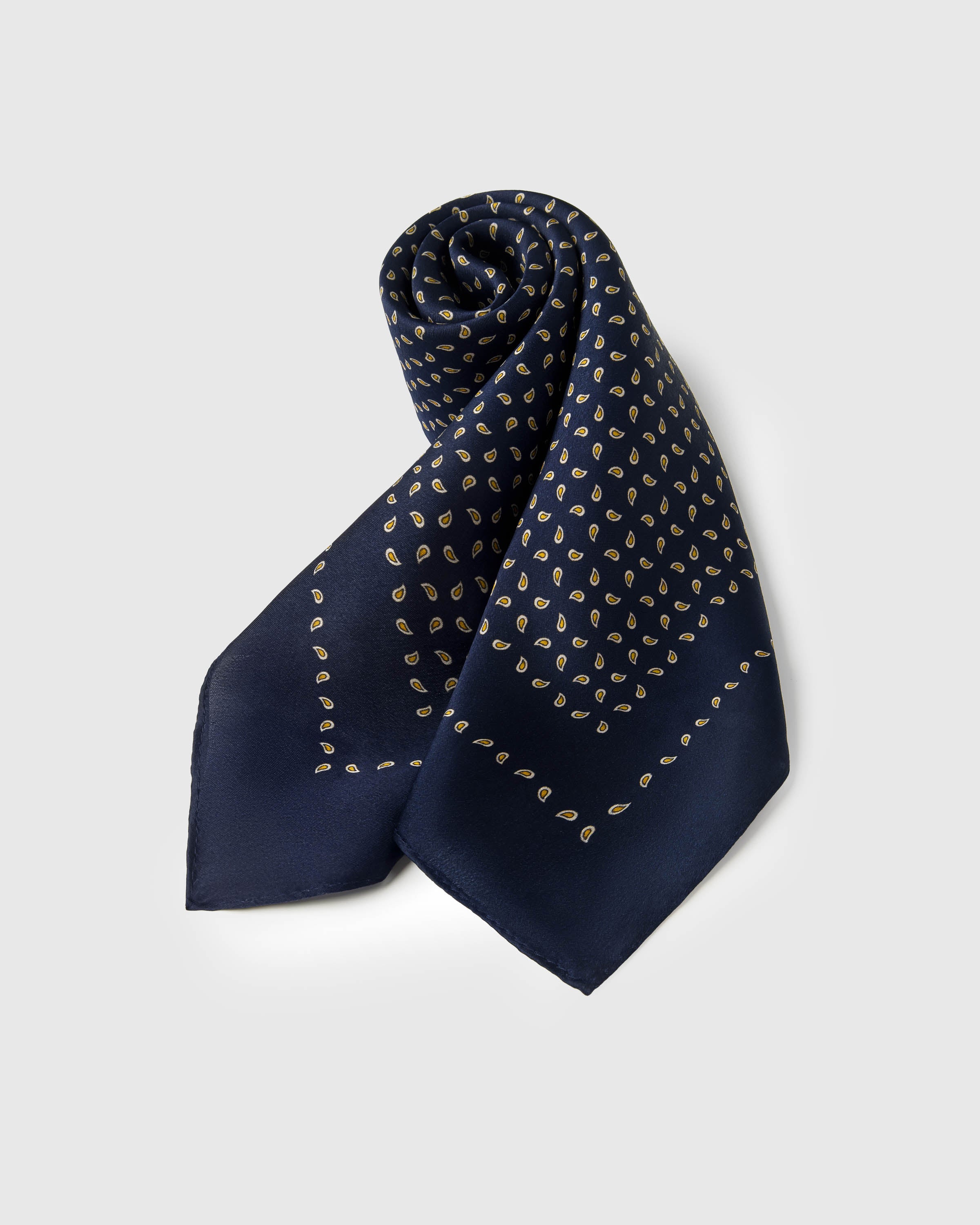 Rolled silk scarf showing the navy paisley field meeting the thin gold border line
```