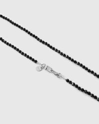 Close-up of two strands of faceted jet-black beads meeting the silver-tone dual clasp and round engraved STICKYZOO disc.