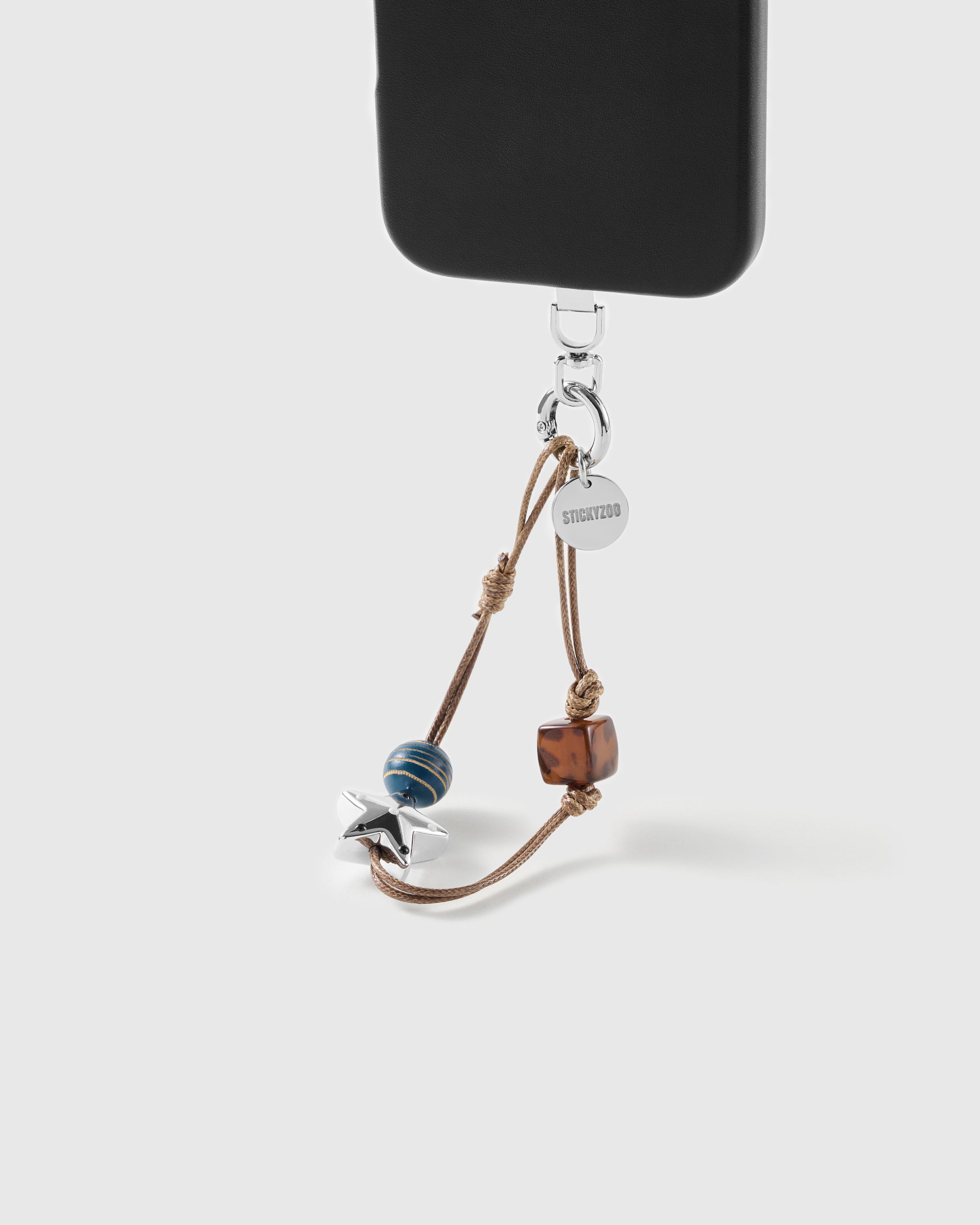 STICKYZOO beaded strap on a black phone: gold-striped blue bead, silver-tone star charm and tortoiseshell cube on tan waxed cord.