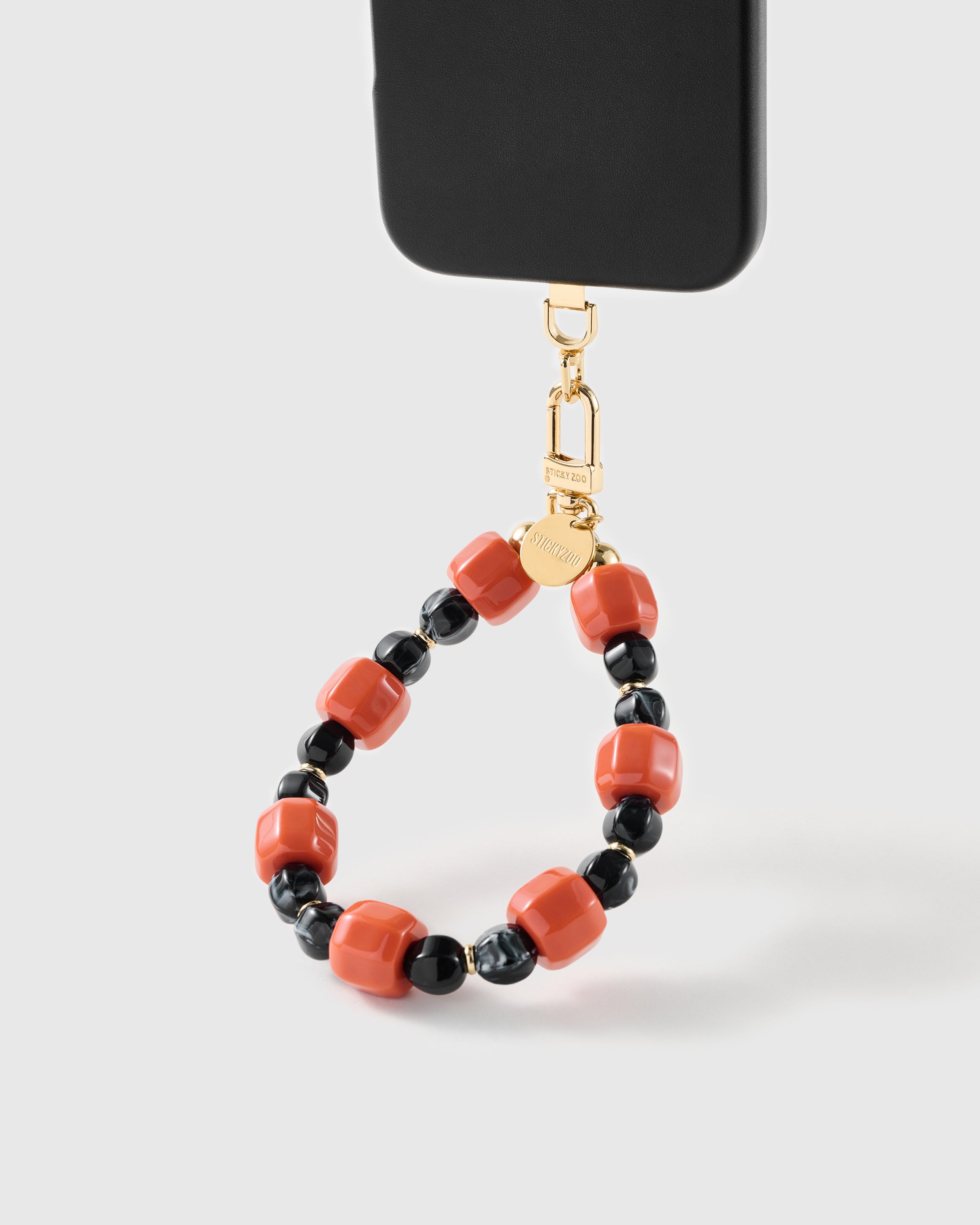 Ember-orange and black bead wrist strap clipped to a black phone case for hands-free carry