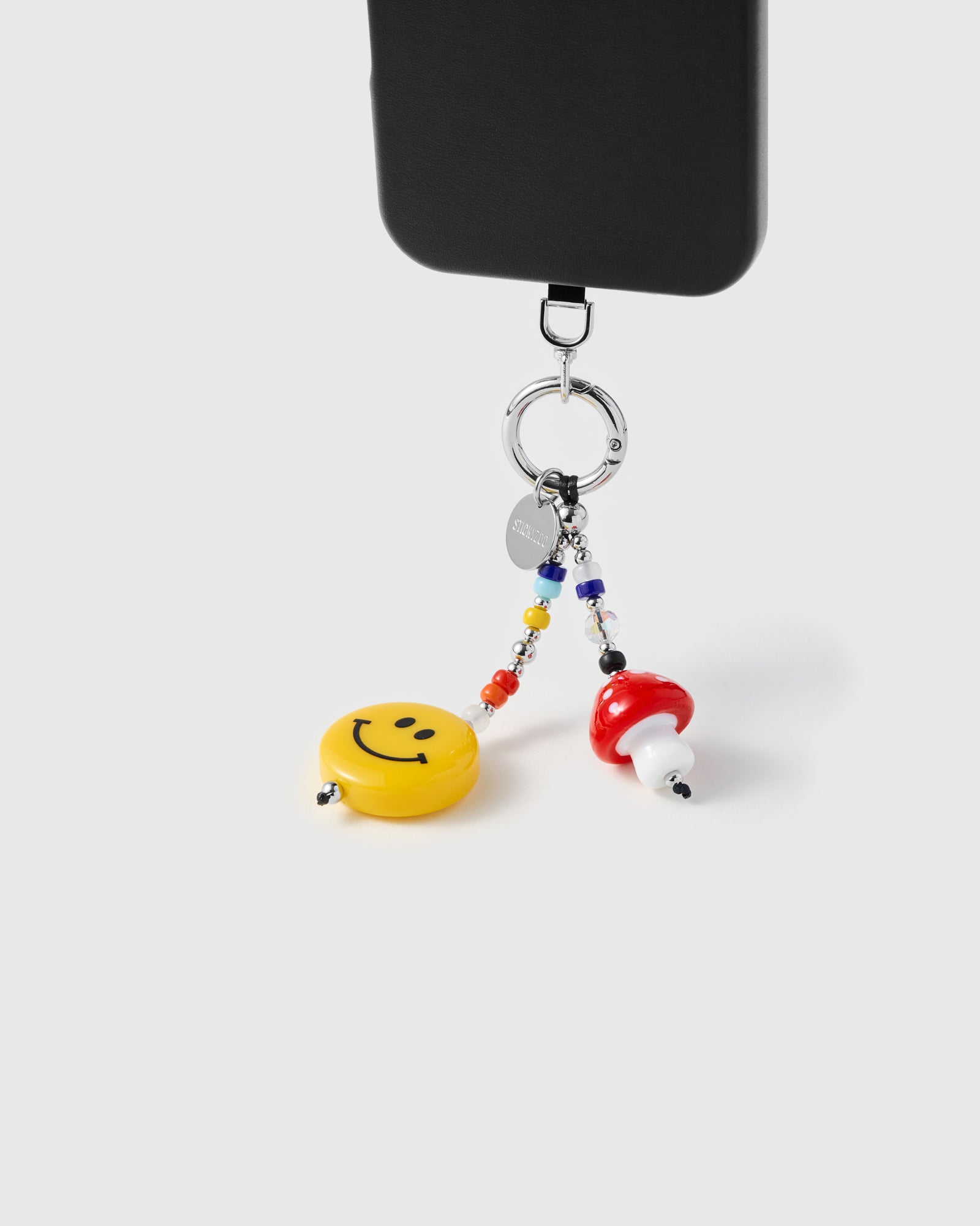 {{Each bead placed by hand}} Smiley face and mushroom charms hanging from phone with rainbow seed beads and silver ring clasp visible