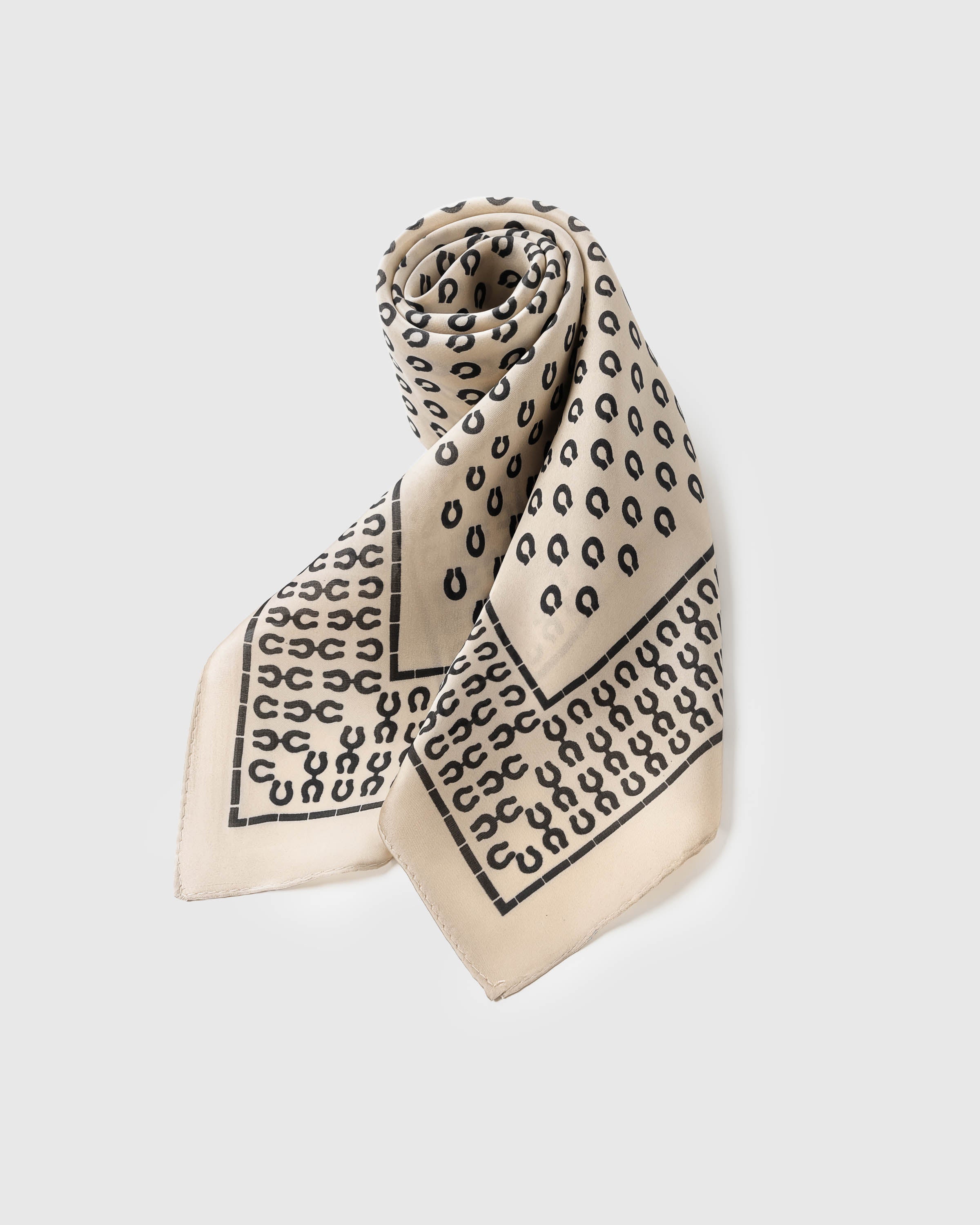 Folded silk scarf rolled along the diagonal showing the horseshoe field meeting the grid-framed border
```