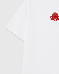 Detail of the raised crab applique near the shoulder showing beaded claws and crystal accents sewn onto white cotton.