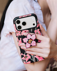 Phone held with fingers gripping the popped-out orchid MagSafe grip on the back of the case