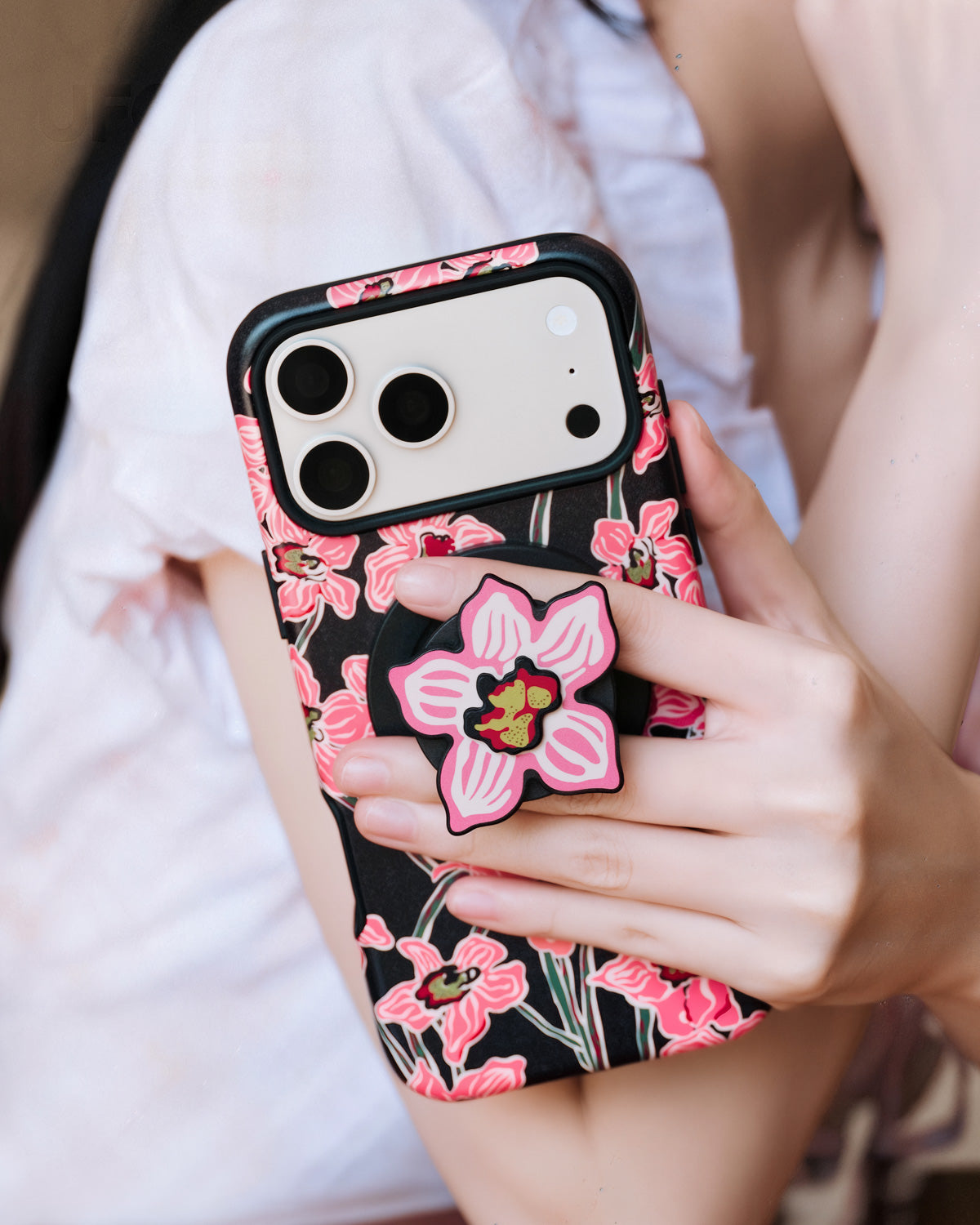 Phone held with fingers gripping the popped-out orchid MagSafe grip on the back of the case