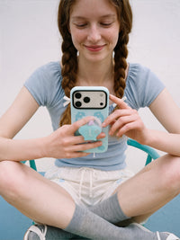 Phone held with fingers gripping the retractable MagSafe pop-grip on the back of the dolphin cove case