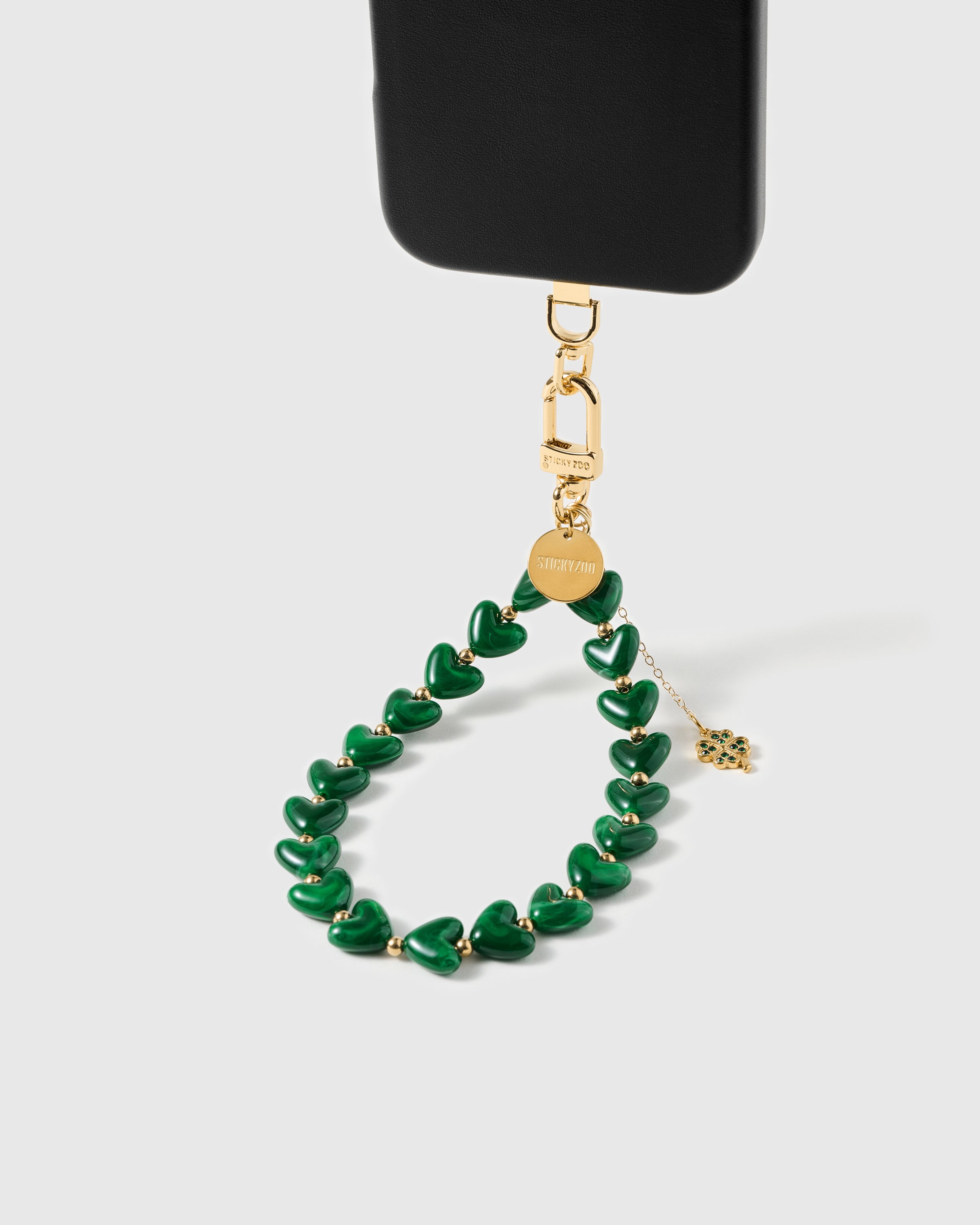 LUCKY CHARM ON YOUR PHONE — Emerald clover heart strap hanging from phone case showing gold clover drop and emerald beads — Loved by Thousands