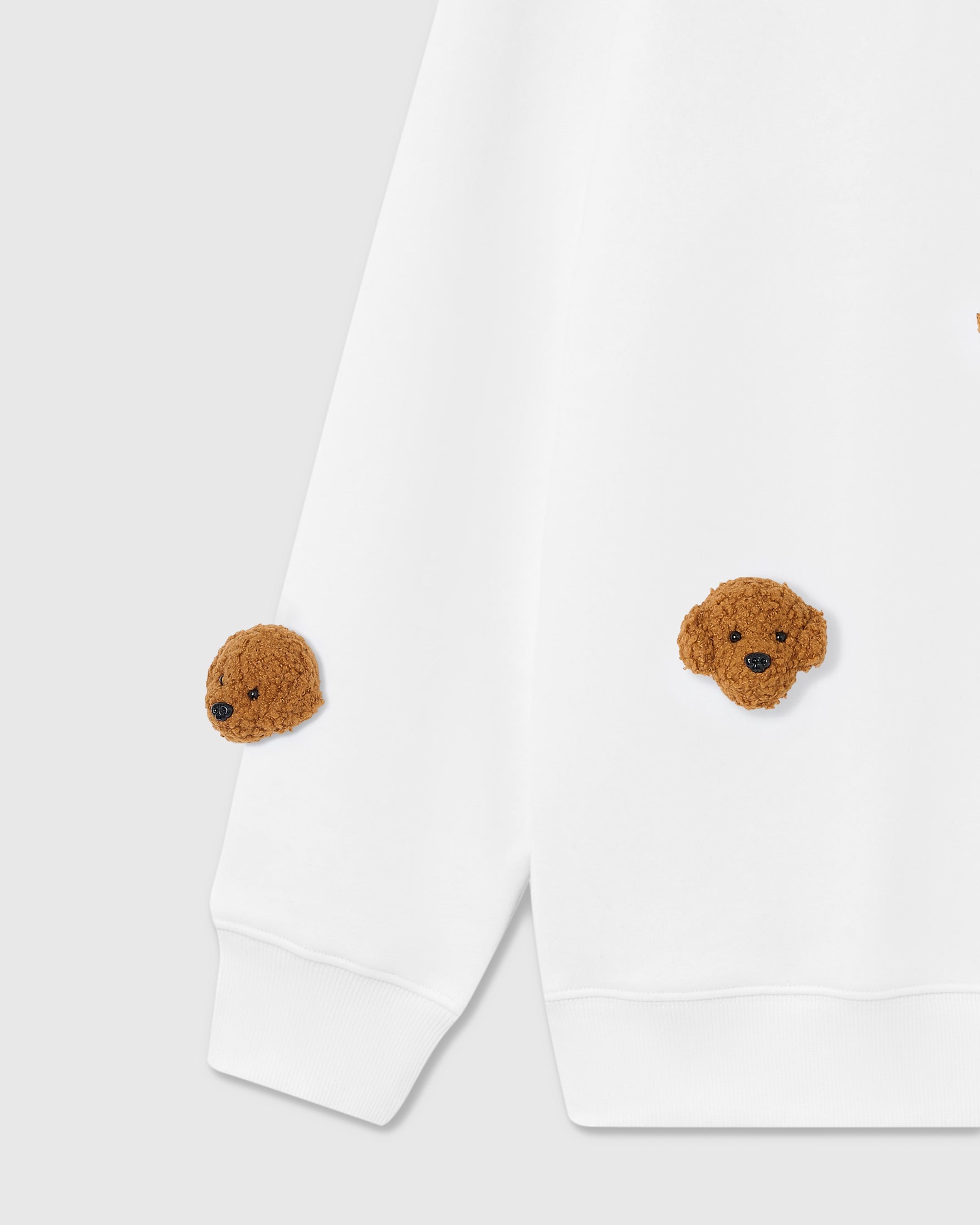 Detail view of three plush poodle faces on white cotton showing dimensional texture and individual stitching