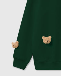 Detail of three plush teddy bear faces on forest green cotton showing dimensional depth and individual stitching