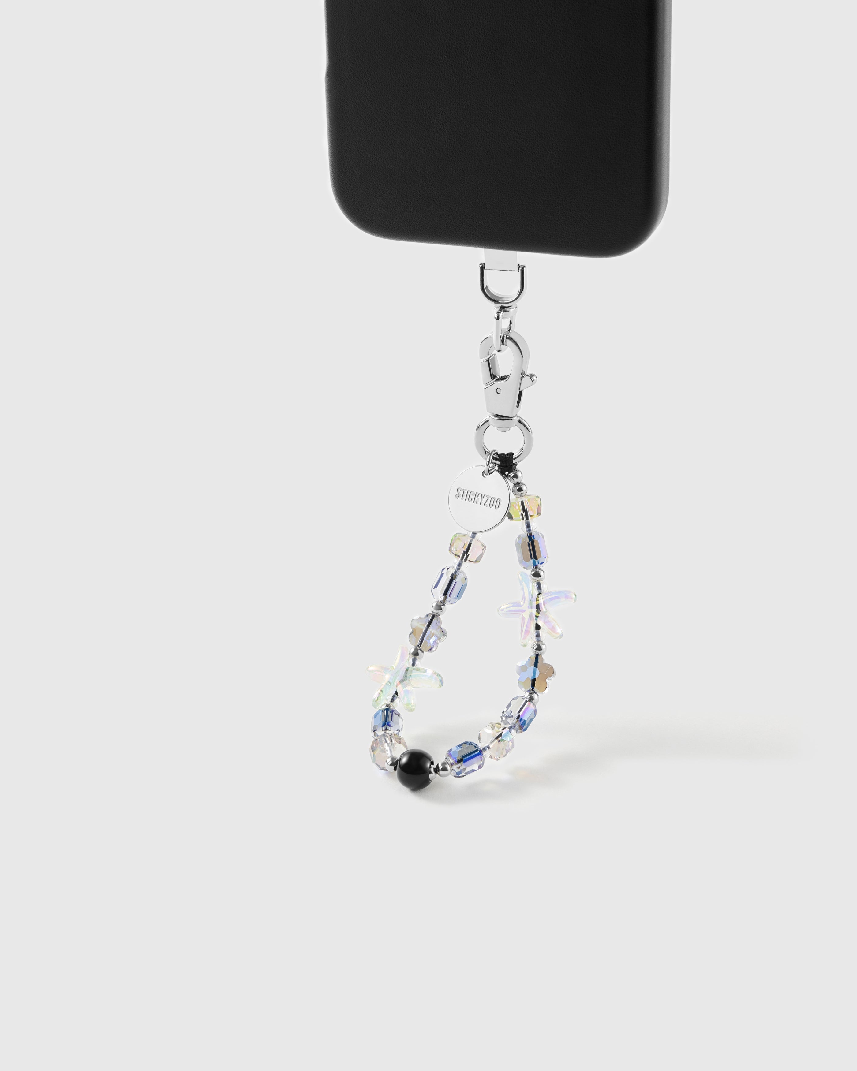 Aurora Starfish beaded strap hanging from a black phone case by its silver clasp, with the engraved STICKYZOO disc and a glossy black bead