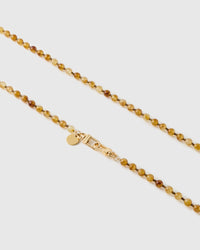 Close-up of glossy amber and honey resin beads, marbled tones with tiny bronze spacers, meeting gold-tone dual clasps and a small engraved disc.