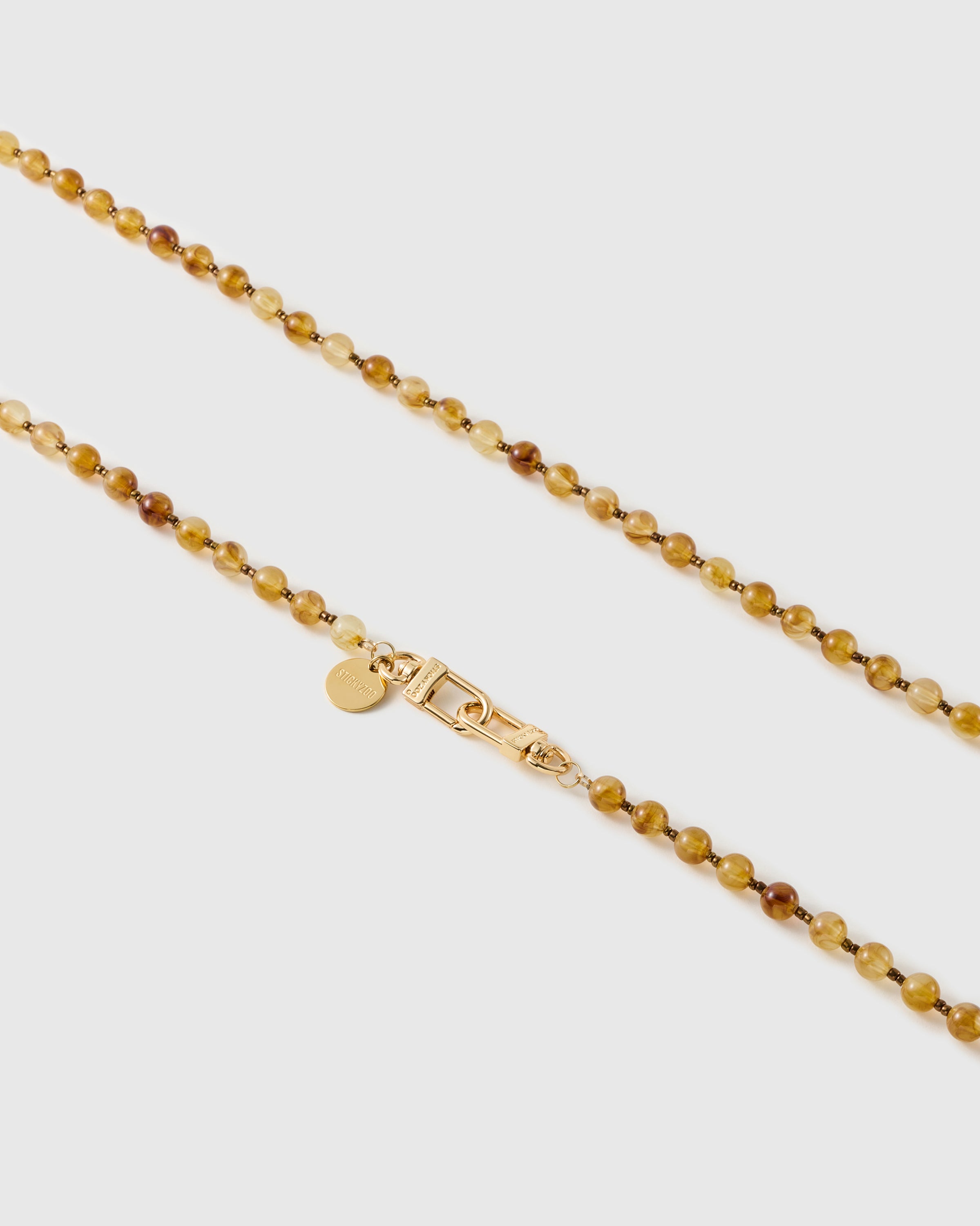 Close-up of glossy amber and honey resin beads, marbled tones with tiny bronze spacers, meeting gold-tone dual clasps and a small engraved disc.