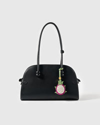 STICKYZOO pitaya leather charm hanging from a black structured shoulder bag showing magenta skin, cream flesh, and green sepals