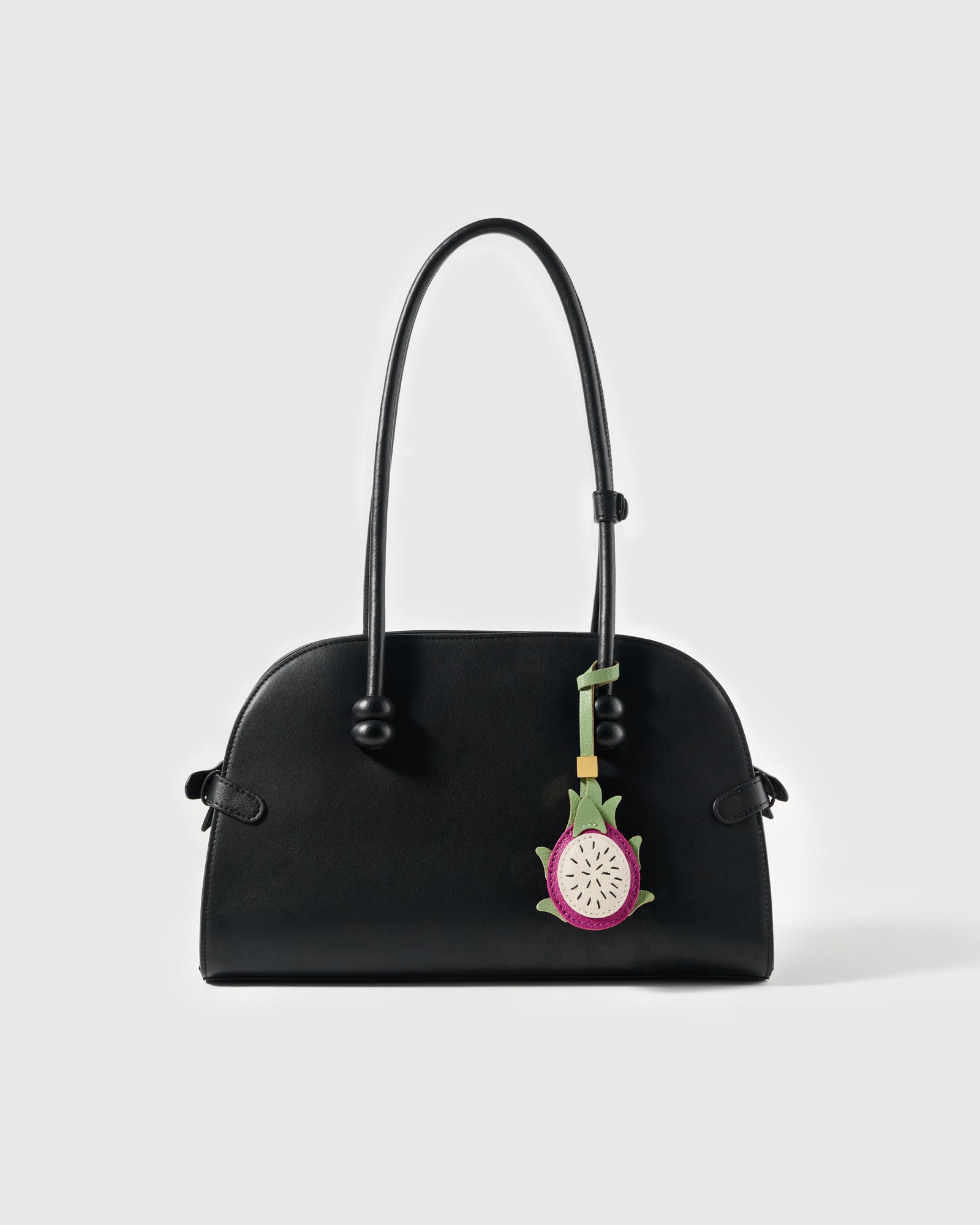 STICKYZOO pitaya leather charm hanging from a black structured shoulder bag showing magenta skin, cream flesh, and green sepals