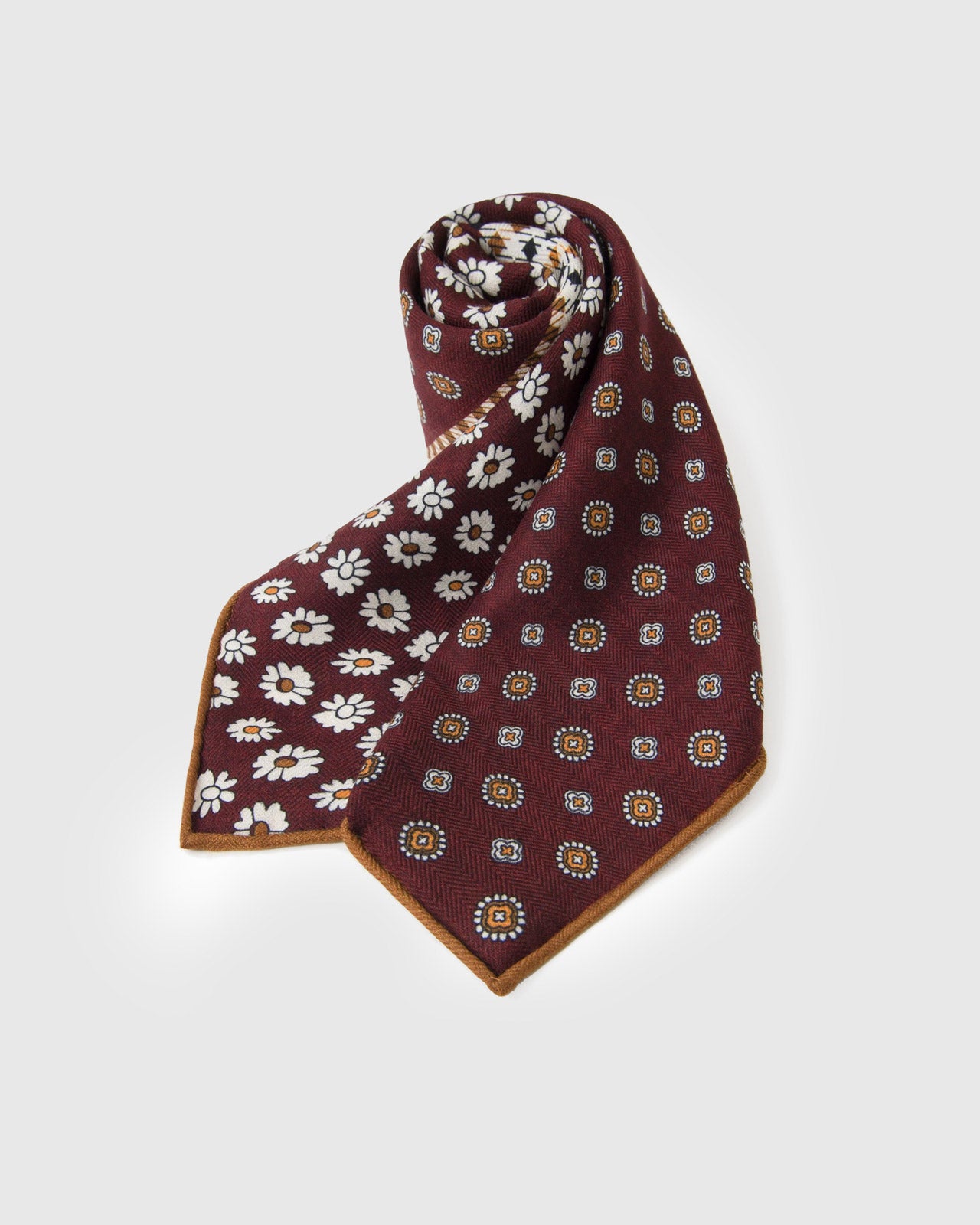 Rolled oxblood silk scarf showing the patchwork motif and thin caramel edge framing the print
```