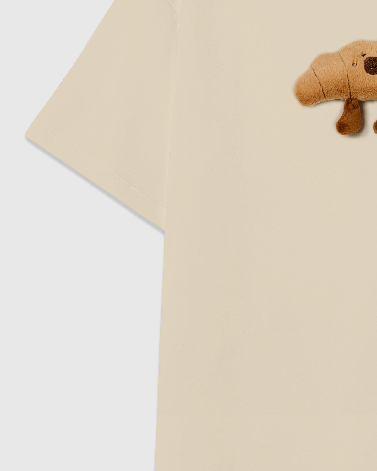 {{Each one sewn by hand}} Detail of sleeve and side on STICKYZOO beige Runaway Croissant T-Shirt showing boxy construction