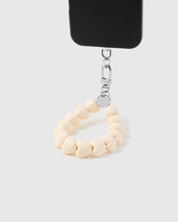 Cream heart bead phone strap hanging from black phone case showing wrist carry