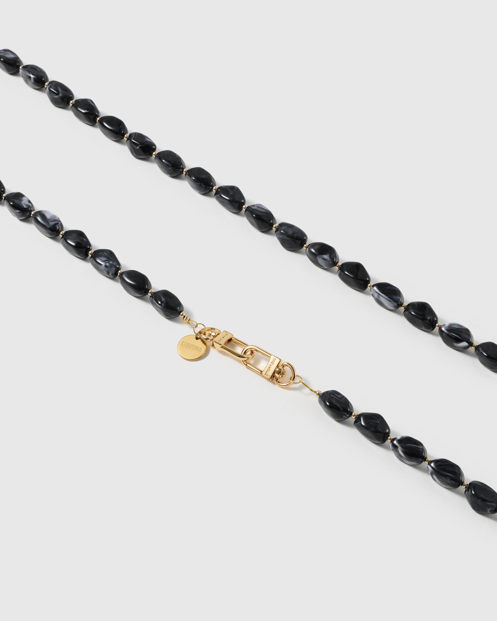 Macro close-up of polished black resin nugget beads and gold-plated clasp on the handmade NOIR ORBIT cross-body strap