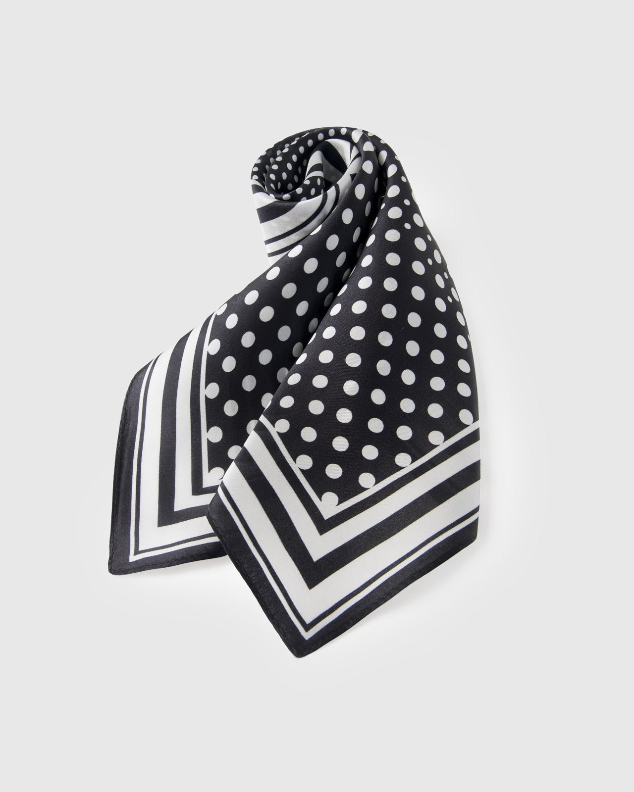 Black and white polka-dot silk scarf rolled and knotted to show the small-square format and graphic frame
```