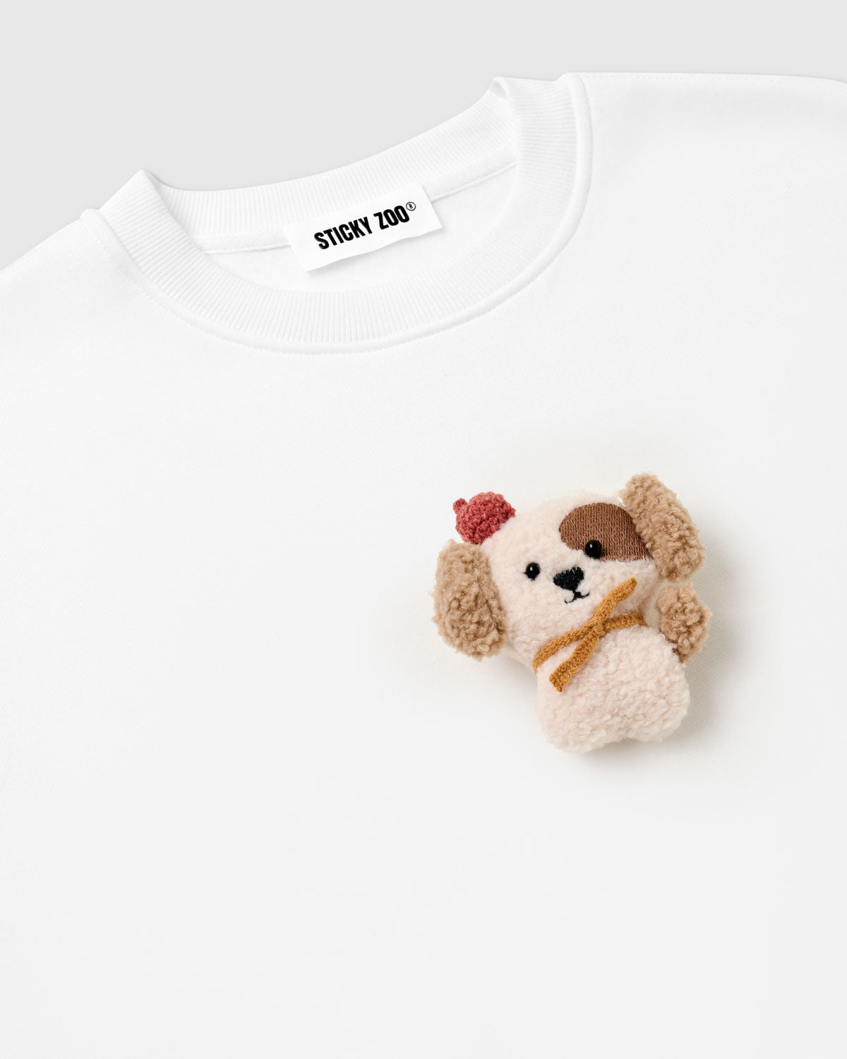 {{Rated 4.9 by thousands}} Close-up of 3D plush puppy with floppy tan ears and golden scarf on STICKYZOO white sweatshirt