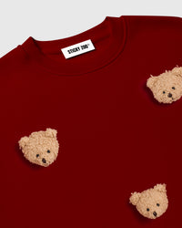 Detail of upper chest area on red Sticky Bear Sweatshirt showing plush bear placement near ribbed crew neck